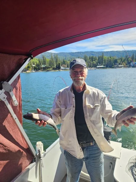 Mike Beighey holding two freshly caught rainbow trout aboard his fishing boat on Bass Lake